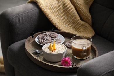 Photo of Wooden tray with delicious breakfast and beautiful flower on armchair indoors