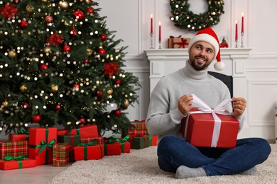 Photo of Happy young man in Santa hat opening Christmas gift at home
