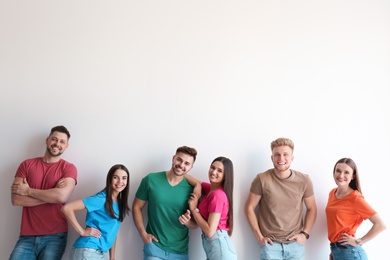 Photo of Group of happy people posing near light wall, space for text