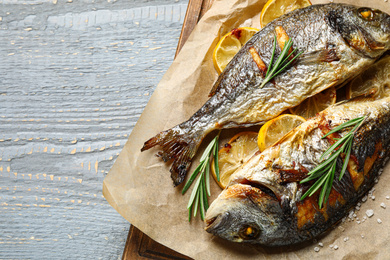 Photo of Delicious roasted fish with lemon on grey wooden table, top view