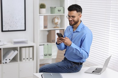 Photo of Handsome young man using smartphone in office, space for text