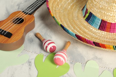 Photo of Mexican sombrero hat, ukulele and maracas on grey textured table, closeup