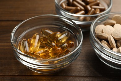 Different dietary supplements in glass bowls on wooden table, closeup