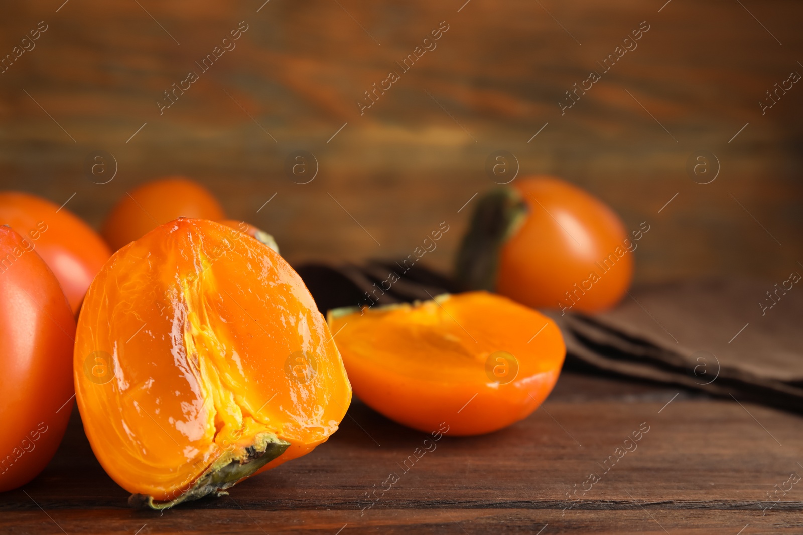 Photo of Delicious fresh persimmons on brown wooden table, closeup