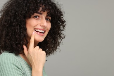 Young woman showing her teeth with whitening strip on grey background, space for text