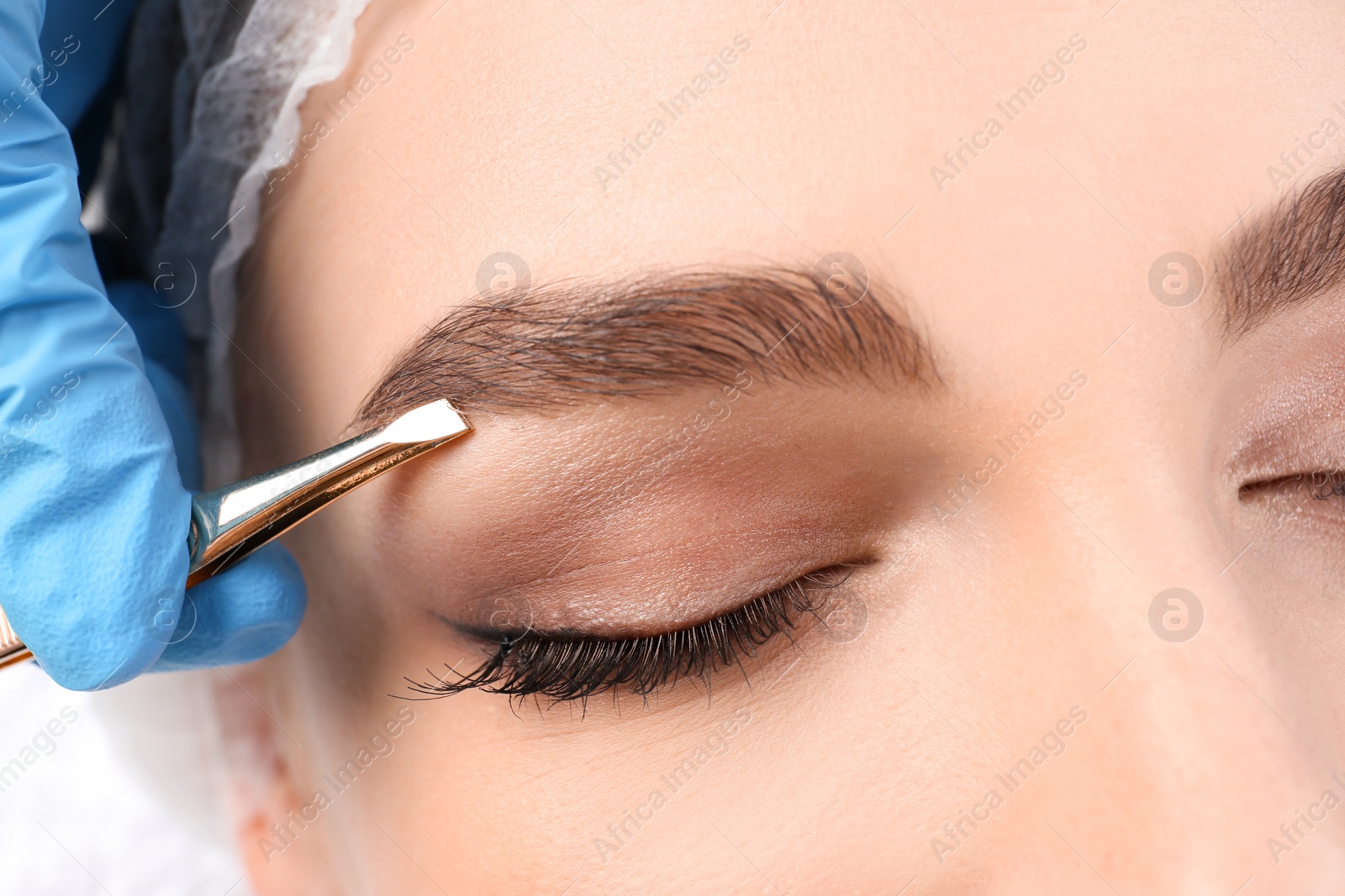 Photo of Young woman having professional eyebrow correction procedure in beauty salon