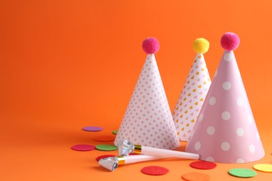 Photo of Party hats and other bright decor elements on orange background, space for text