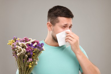 Photo of Allergy symptom. Man with bunch of flowers sneezing on light grey background