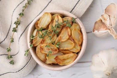 Photo of Fried garlic cloves with thyme in bowl on white table, flat lay