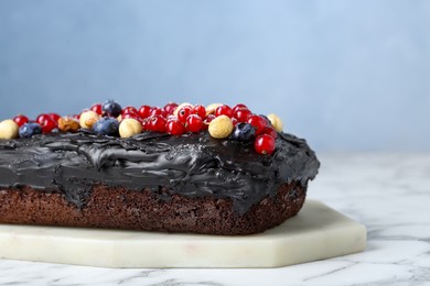 Photo of Delicious chocolate sponge cake with berries and nuts on white marble table, closeup