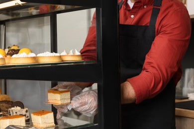 Worker taking tasty piece of cheesecake with jelly from showcase in cafe, closeup