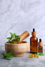 Photo of Wooden mortar with fresh green herbs, extracts and capsules on light grey table