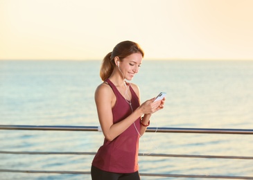 Young woman choosing music for fitness exercises on pier in morning