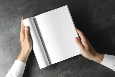 Man holding blank notebook at black textured table, top view. Mockup for design