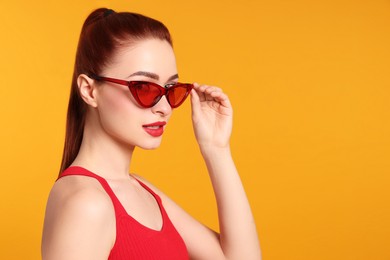Beautiful woman with red dyed hair and sunglasses on orange background, space for text