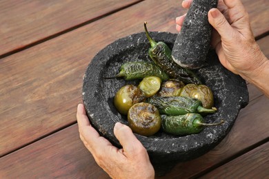 Photo of Woman grinding vegetables in mortar at wooden table, closeup. Ingredients for salsa sauce