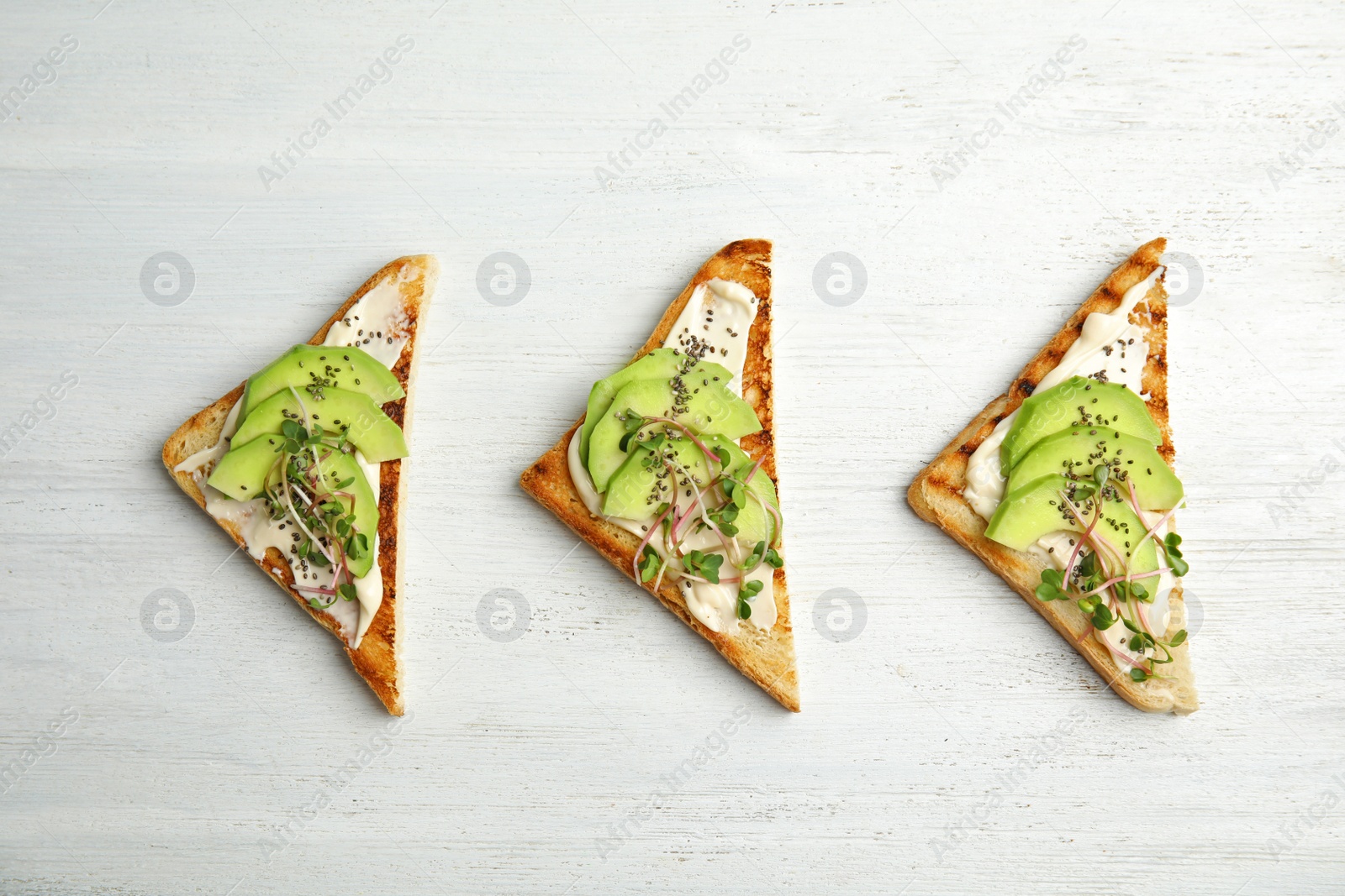 Photo of Tasty toasts with avocado, sprouts and chia seeds on white wooden background, top view