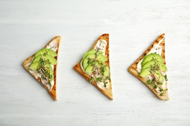 Tasty toasts with avocado, sprouts and chia seeds on white wooden background, top view