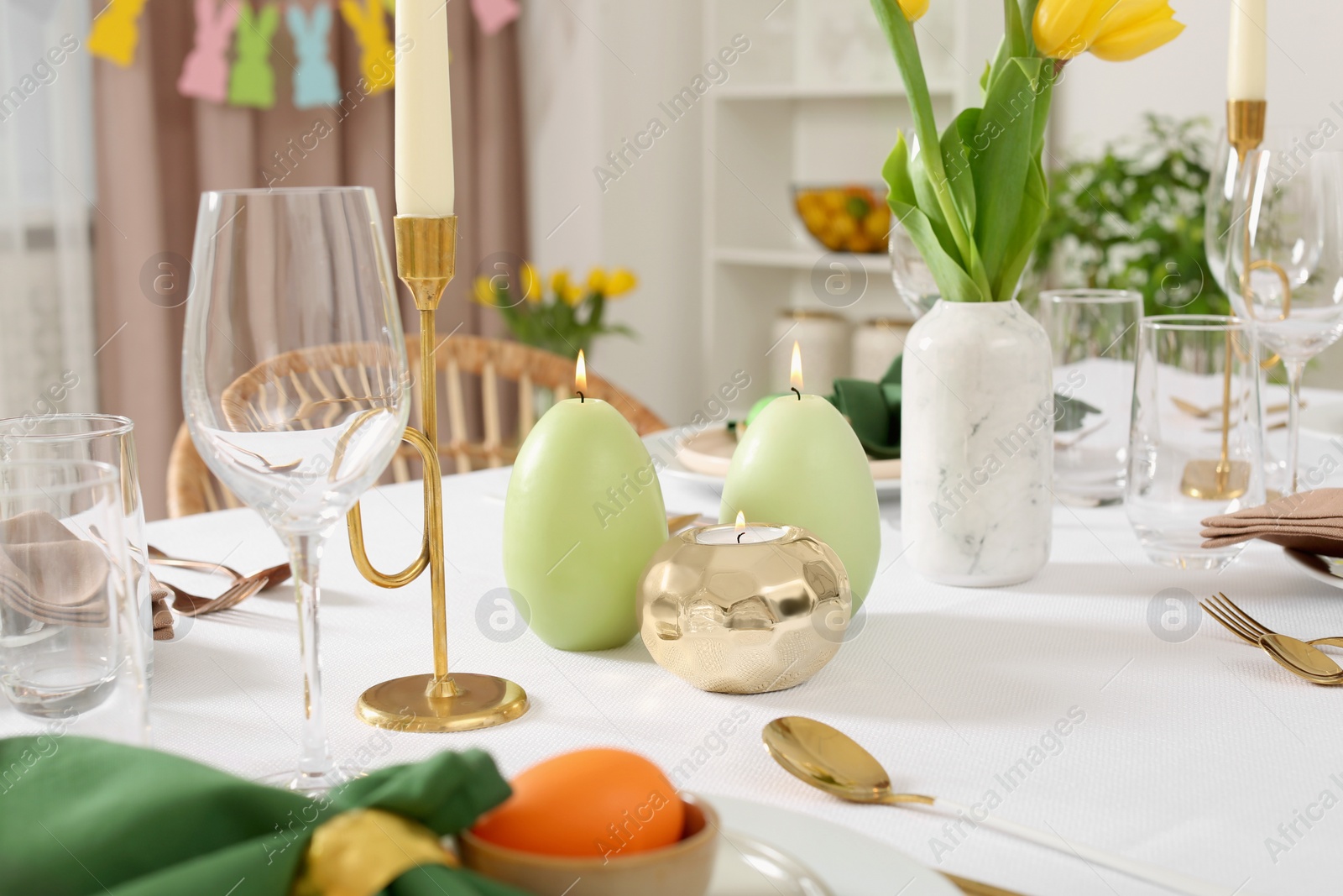 Photo of Festive Easter table setting with painted eggs, burning candles and yellow tulips indoors