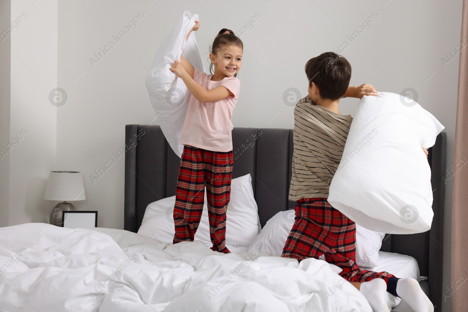 Photo of Brother and sister having pillow fight while changing bed linens in bedroom