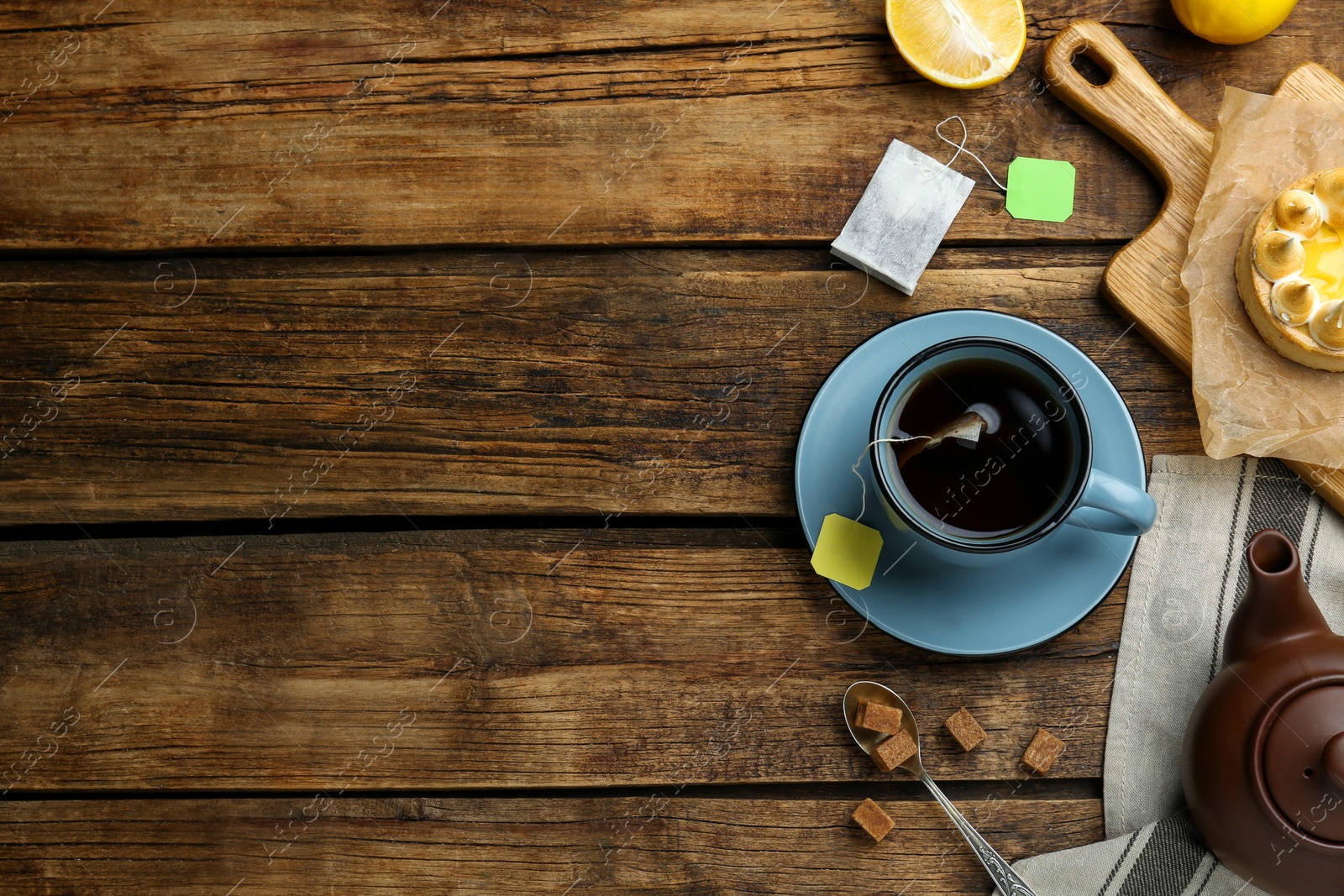 Photo of Flat lay composition with tea bag in cup of hot water on wooden table, space for text