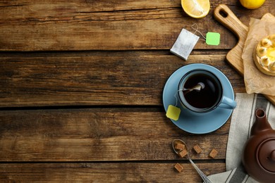 Photo of Flat lay composition with tea bag in cup of hot water on wooden table, space for text