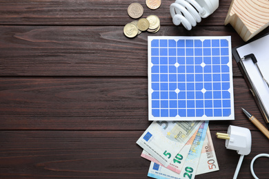 Photo of Flat lay composition with solar panel and money on wooden table. Space for text