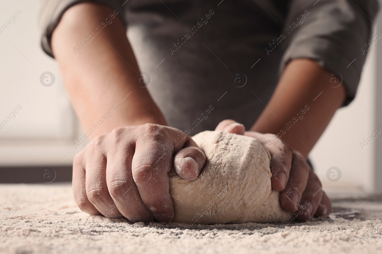 Photo of Man kneading dough at table in kitchen, closeup