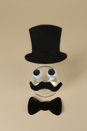 Photo of Man's face made of fake mustache, ball, hat, bow tie and eyes on beige background, top view