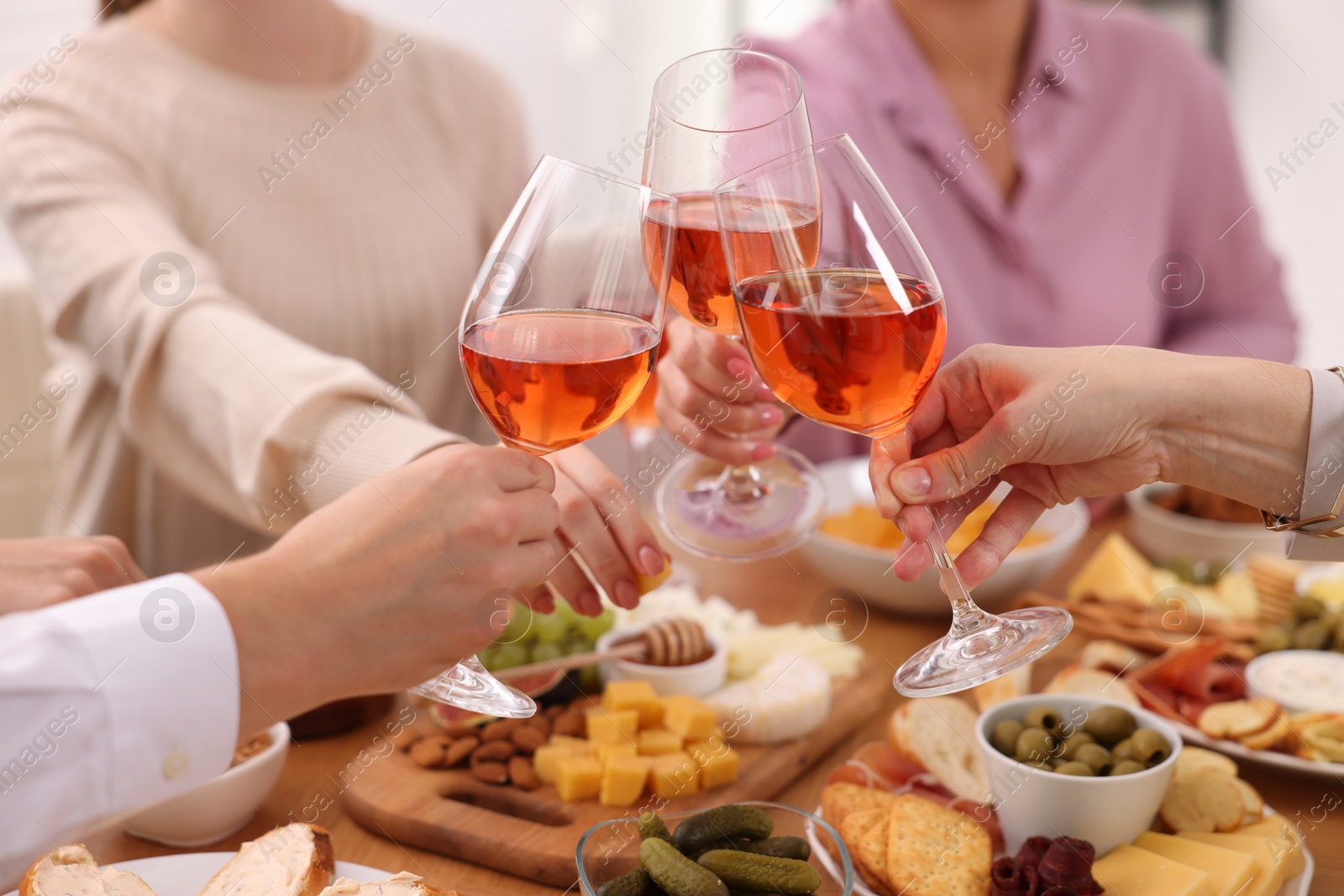 Photo of People clinking glasses with rose wine above table indoors, closeup