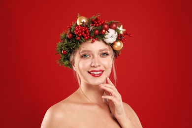 Photo of Beautiful young woman wearing Christmas wreath on red background