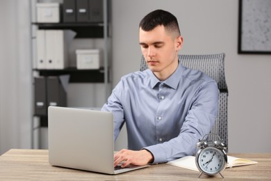 Photo of Man working at wooden table, focus on alarm clock