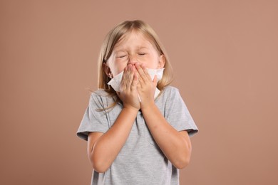 Photo of Suffering from allergy. Little girl with tissue sneezing on light brown background
