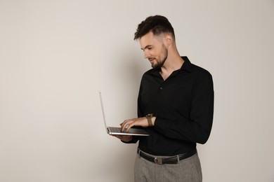 Photo of Handsome man in black shirt working with laptop on light grey background, space for text