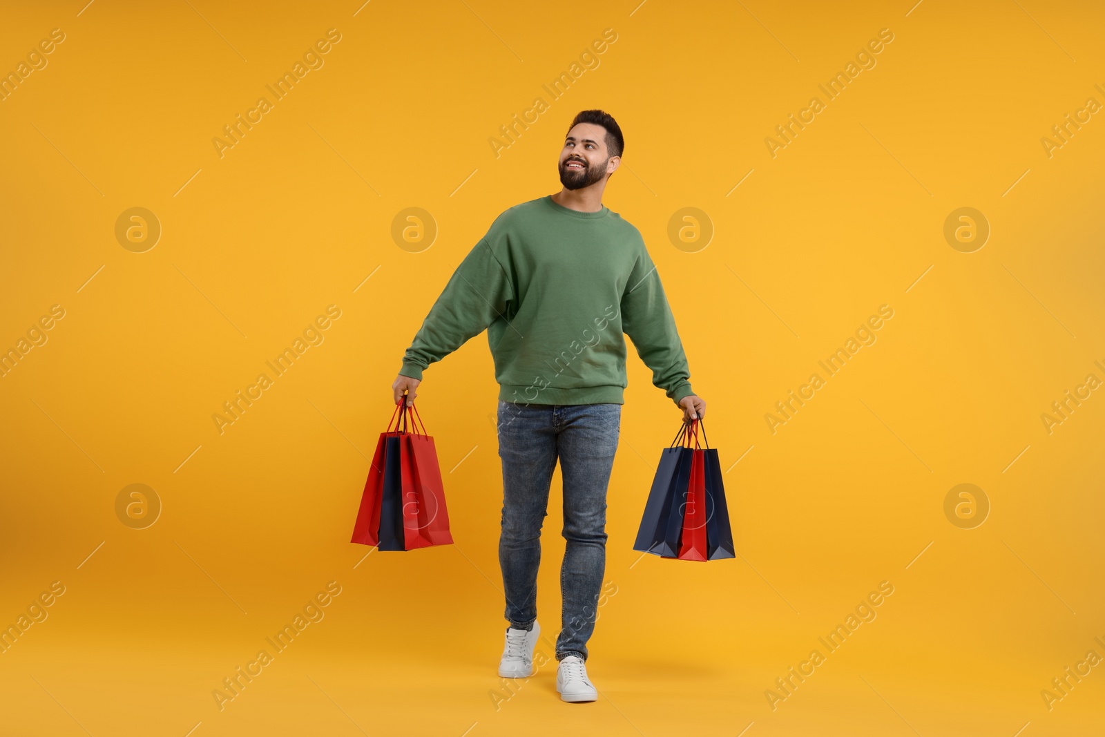 Photo of Smiling man with many paper shopping bags on orange background