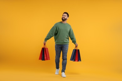 Smiling man with many paper shopping bags on orange background