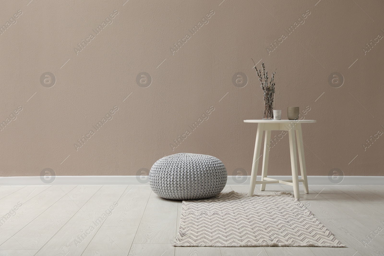 Photo of Knitted pouf and decor elements near beige wall indoors. Space for text