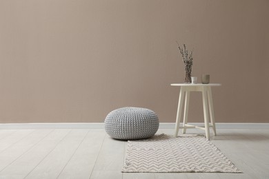 Knitted pouf and decor elements near beige wall indoors. Space for text