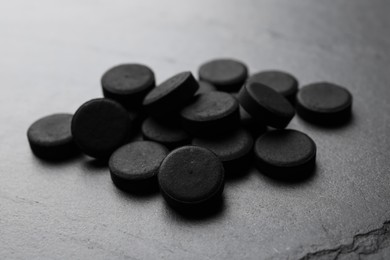 Photo of Pile of activated charcoal pills on black table, closeup. Potent sorbent
