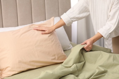 Woman making bed with new pistachio linen in room, closeup