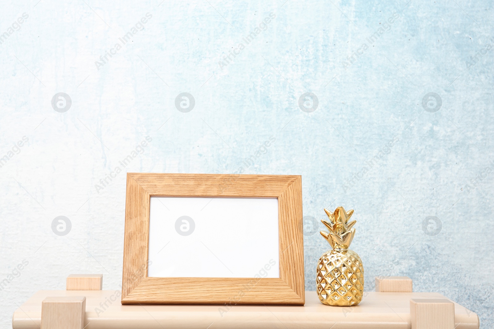 Photo of Blank frame and decorative pineapple figure on table near light wall. Mock up for design