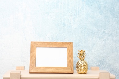 Photo of Blank frame and decorative pineapple figure on table near light wall. Mock up for design