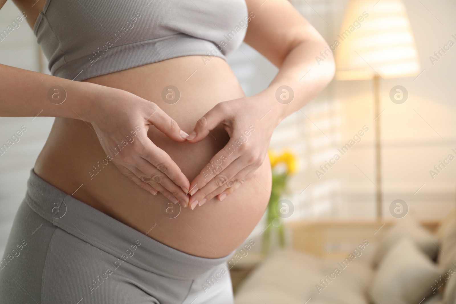 Photo of Pregnant young woman making heart with her hands on belly at home, closeup. Space for text