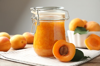 Photo of Jar of apricot jam and fresh fruits on table, closeup