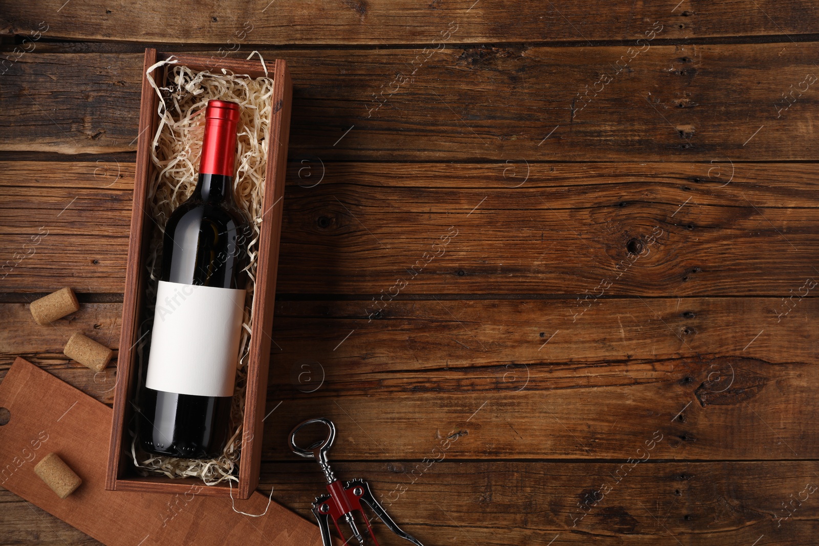 Photo of Box with wine bottle, corkscrew and corks on wooden table, flat lay. Space for text