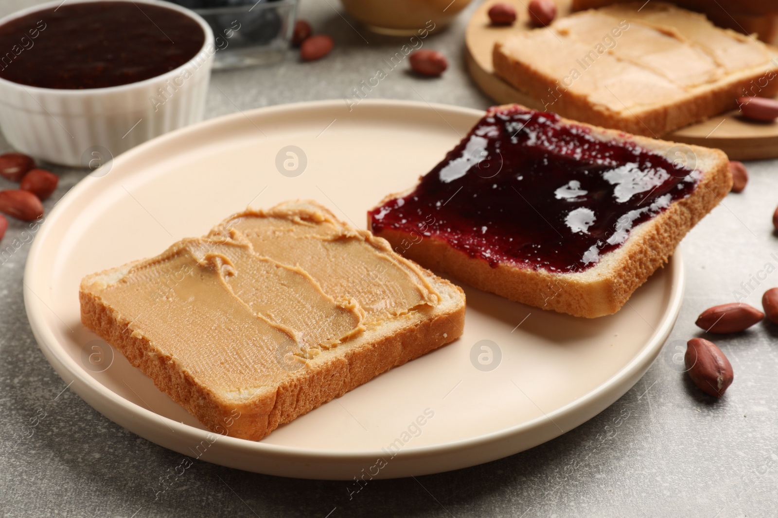 Photo of Tasty peanut butter sandwiches with jam on gray table, closeup