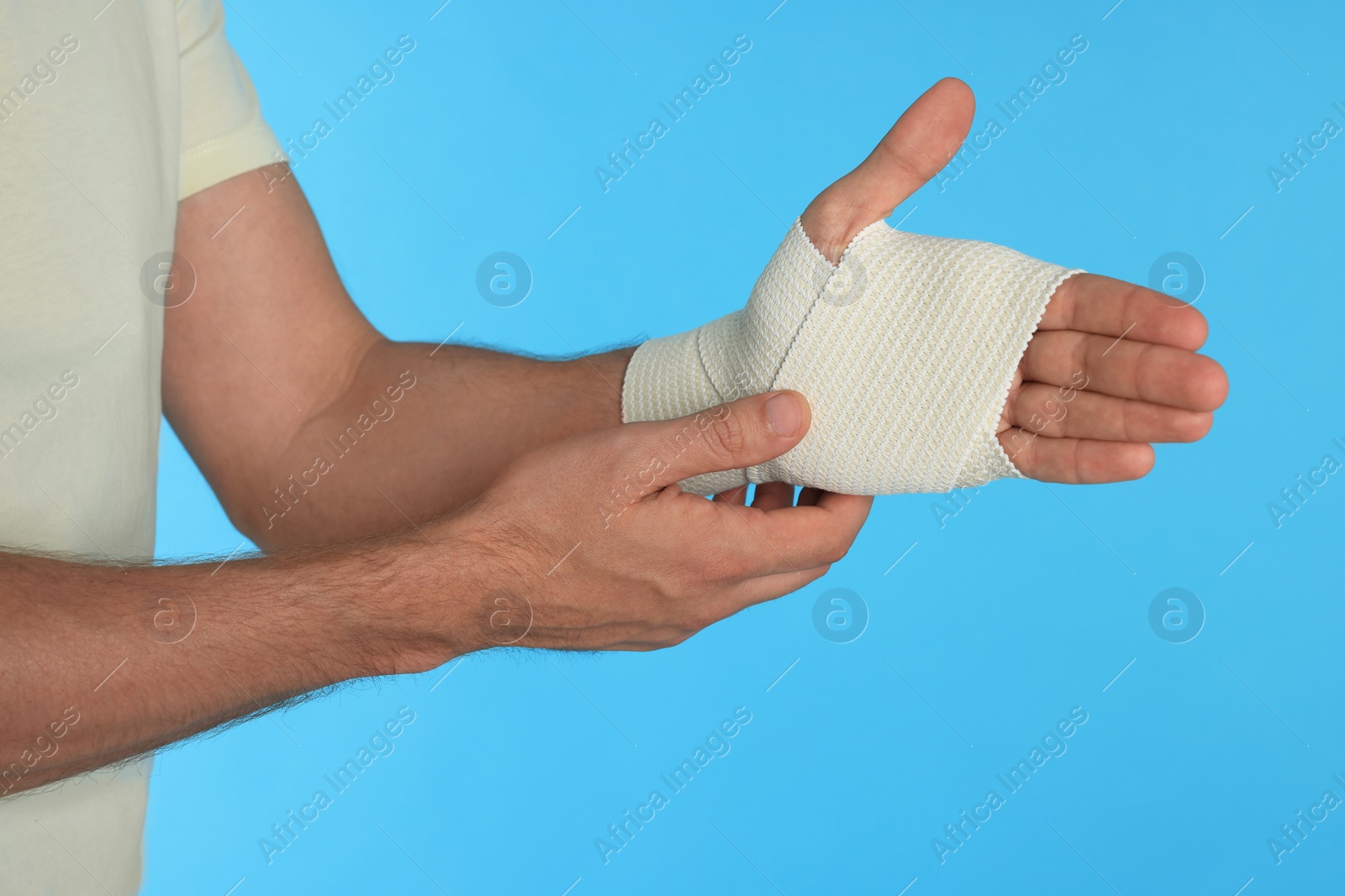 Photo of Man with hand wrapped in medical bandage on light blue background, closeup