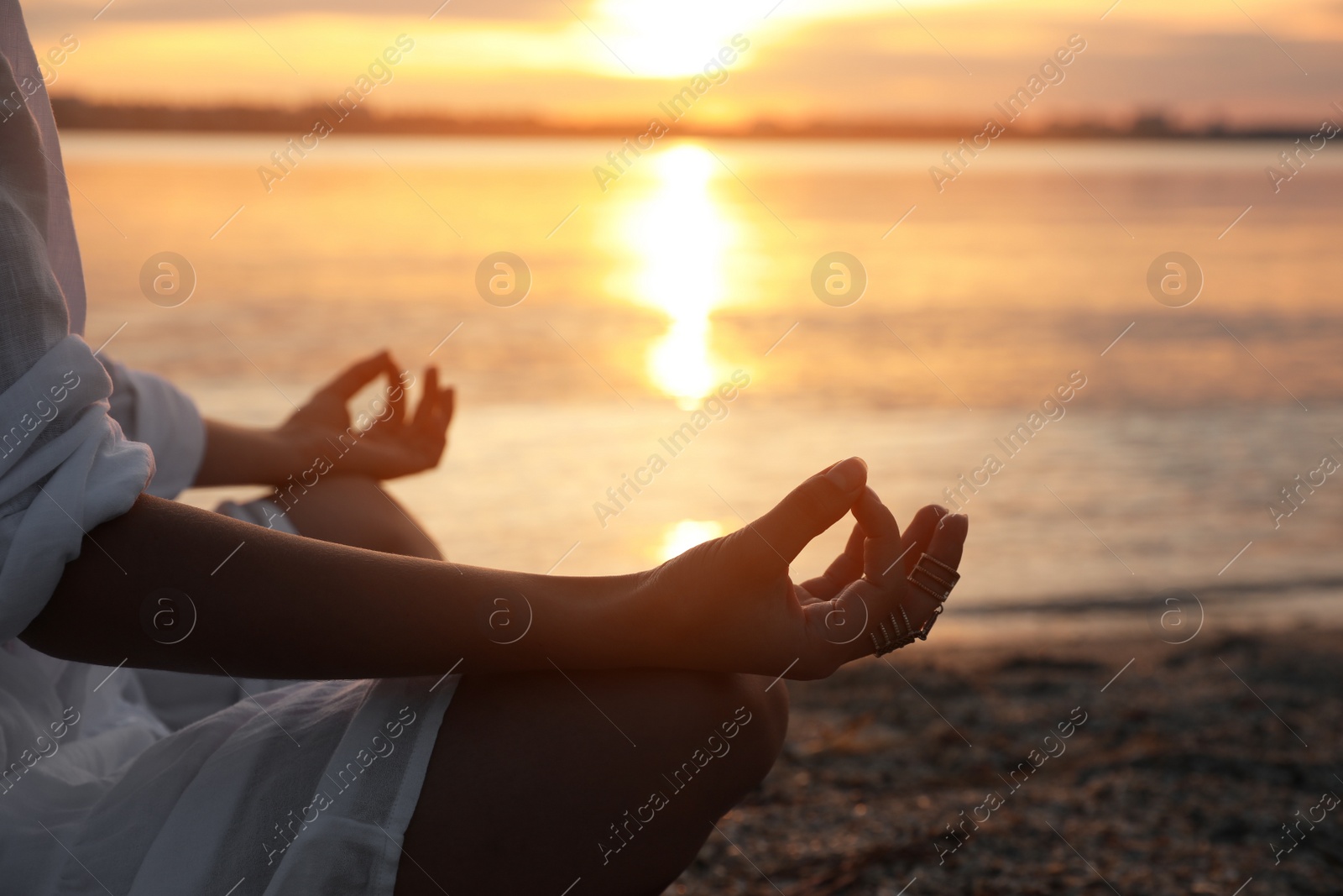 Photo of Young woman meditating near river at sunset, closeup. Nature healing power