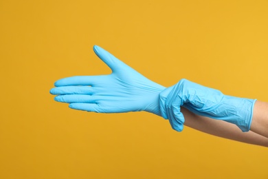 Photo of Doctor wearing medical gloves on yellow background, closeup