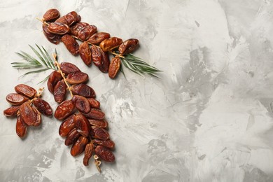 Branches with sweet dried dates and green leaves on light table, flat lay. Space for text